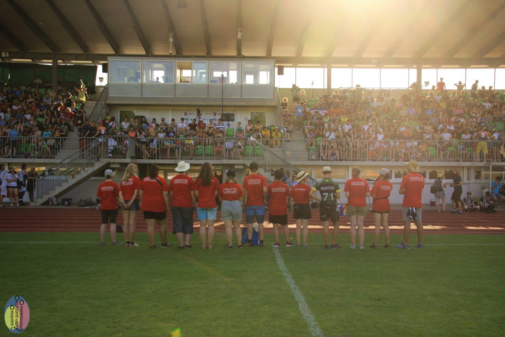 Line of volunteers with their backs to the camera facing a full stadium of fans